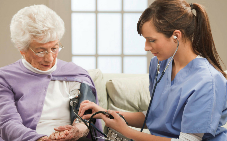 An elderly woman getting her blood pressure checked by a health care assistant