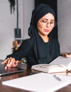 Woman reading a textbook with her hand on a laptop