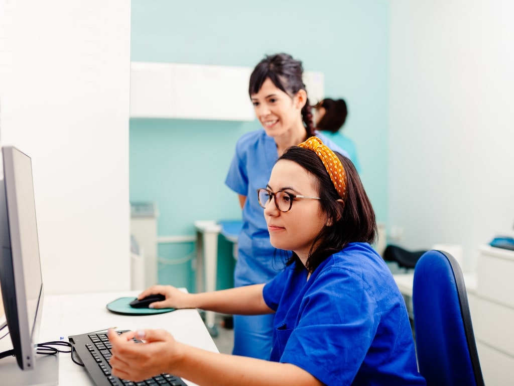 Two health care professionals sit by a desk looking at their desktop computer