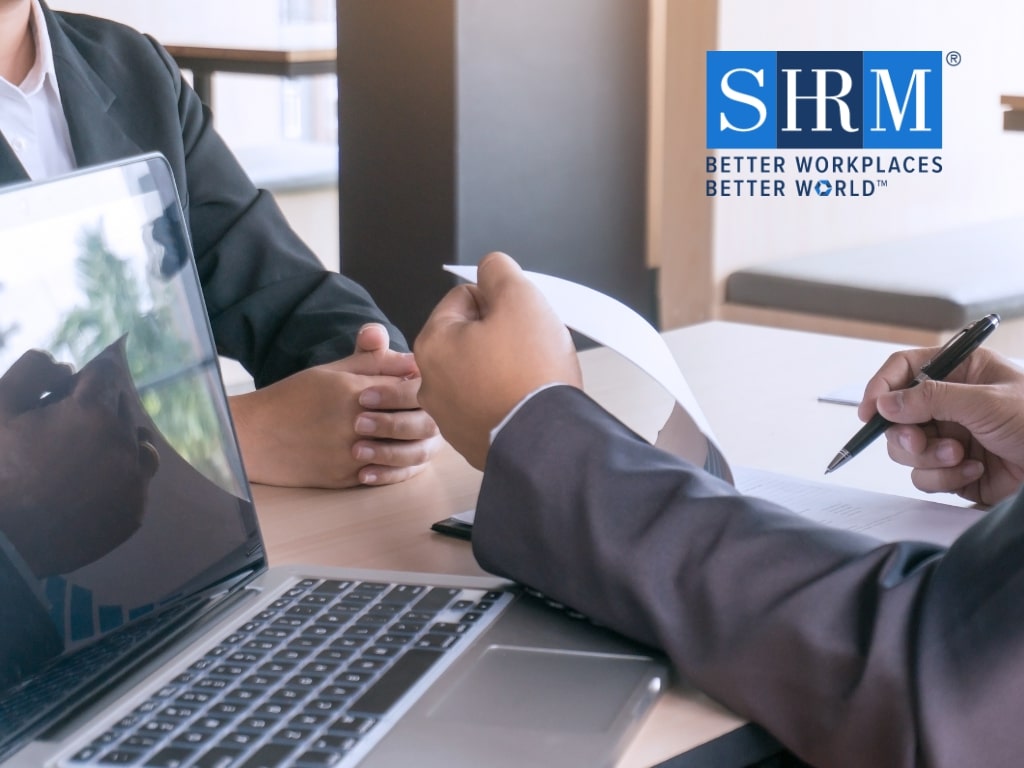 Two people working on paperwork together next to a laptop with the SHRM logo
